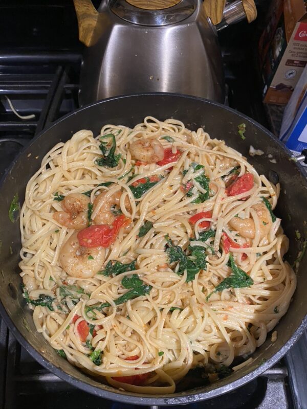 Linguine pasta in a pan with popped cherry tomatoes, shrimp and spinach