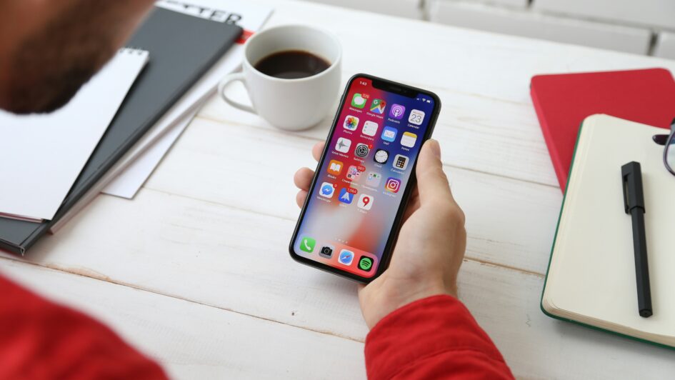 Person sitting and holding their phone with the home page and apps visible