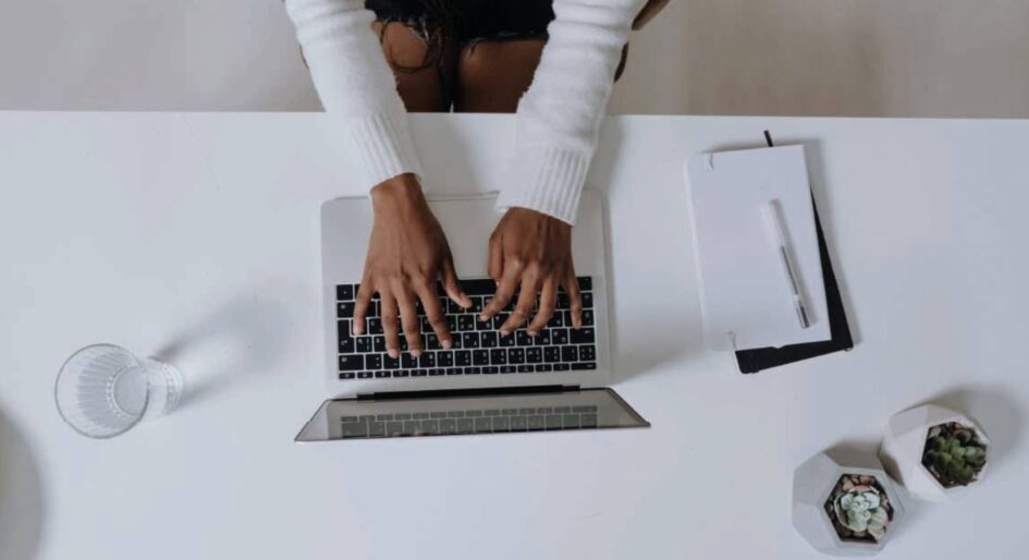 A birds-eye view of someone on their computer with a notepad and pen beside them