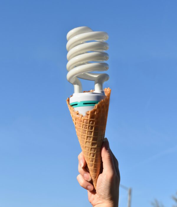 A hand holding an ice cream cone, but instead of ice cream, it's a twisted light bulb