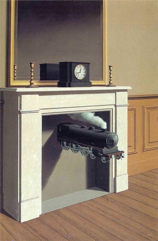 A fireplace mantle with a clock, two candlesticks, and a mirror on it. Where the fireplace should be open for fire, it is sealed shut with a grey wall and coming out of the wall is an old black steam train with smoke coming out the top.